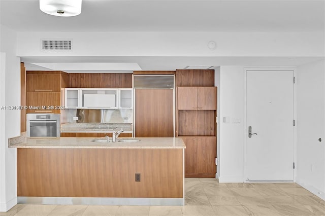 kitchen featuring brown cabinets, paneled built in fridge, stainless steel oven, a peninsula, and visible vents