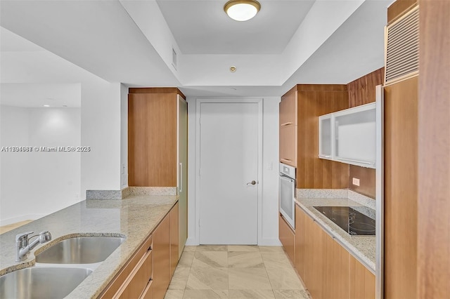 kitchen featuring light stone counters, stainless steel oven, a sink, and modern cabinets