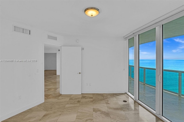 spare room with a water view, floor to ceiling windows, baseboards, and visible vents