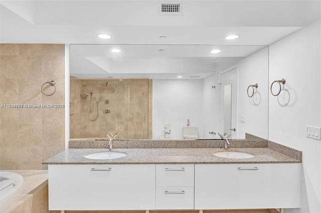 full bathroom with tiled shower, recessed lighting, visible vents, and a sink