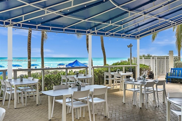 view of patio featuring outdoor dining area, a water view, and a view of the beach