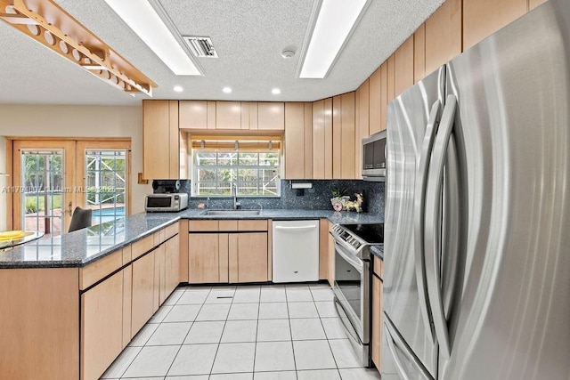 kitchen with visible vents, a sink, a peninsula, stainless steel appliances, and tasteful backsplash