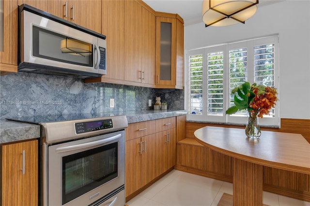 549 NE 12th Ave, Fort Lauderdale, FL 33301 - kitchen with decorative backsplash, brown cabinetry, light countertops, glass insert cabinets, and stainless steel appliances