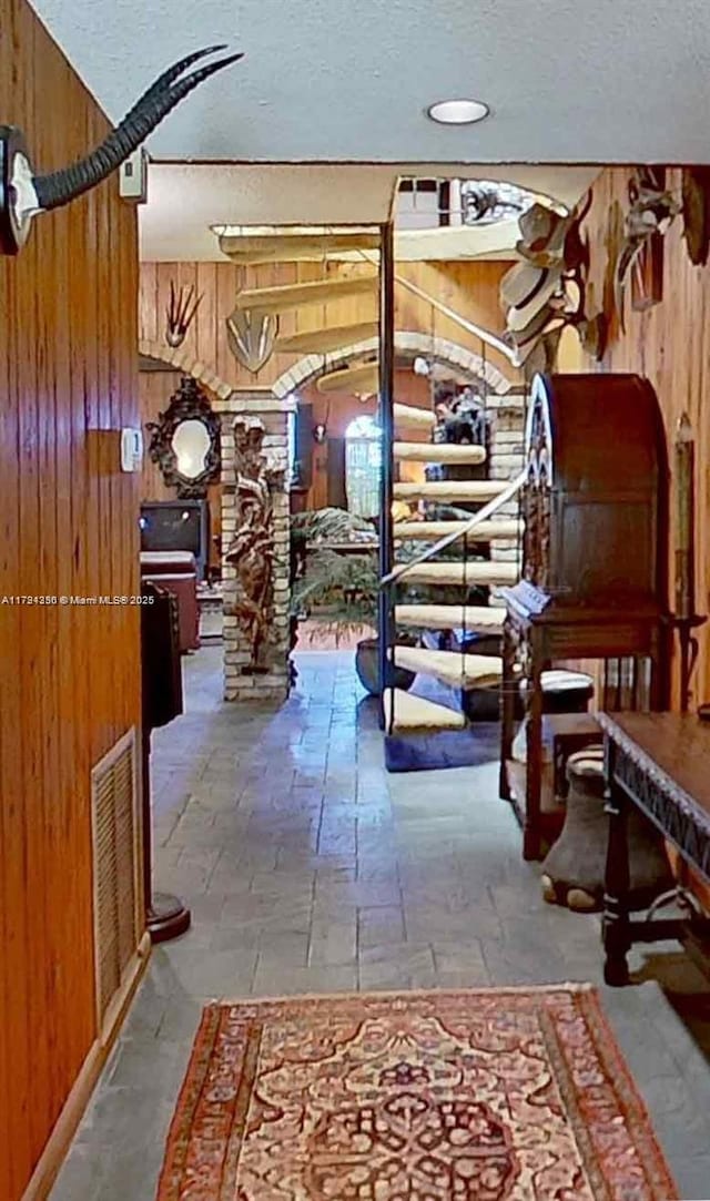 staircase with wooden walls, visible vents, a textured ceiling, and stone tile floors