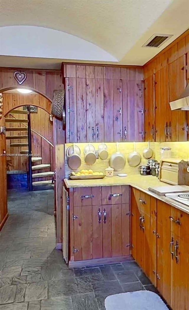 kitchen featuring visible vents, wood walls, exhaust hood, and stone tile flooring