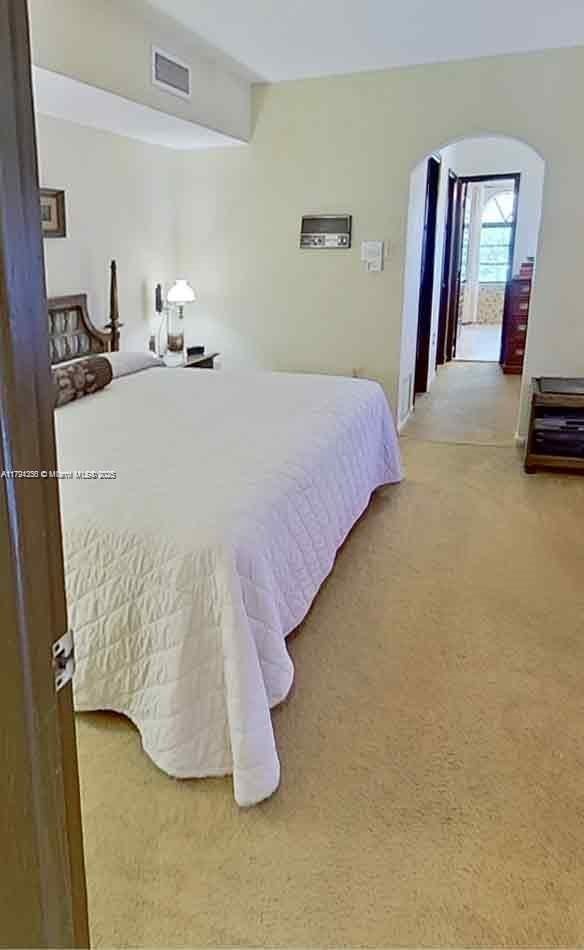 bedroom with arched walkways, carpet, and visible vents