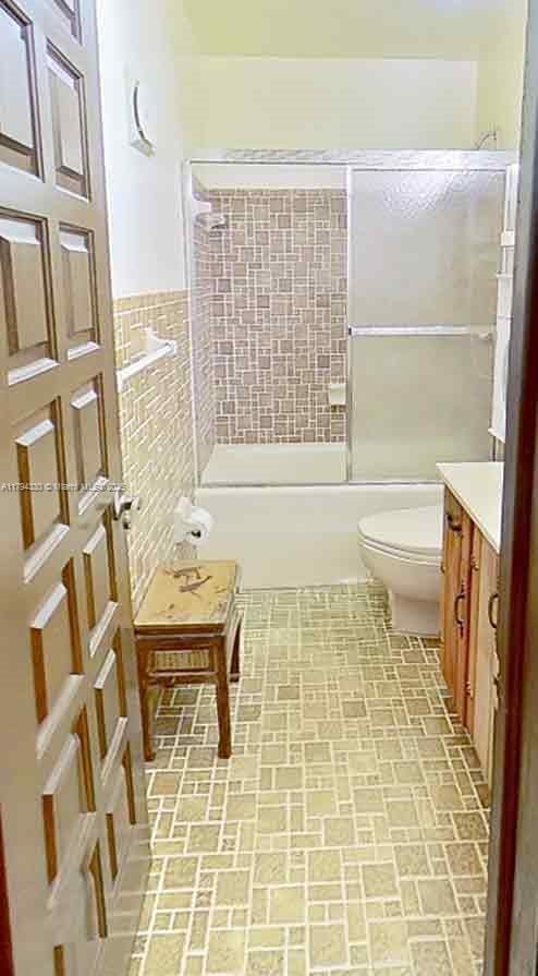 bathroom featuring wainscoting, vanity, toilet, brick patterned floor, and combined bath / shower with glass door
