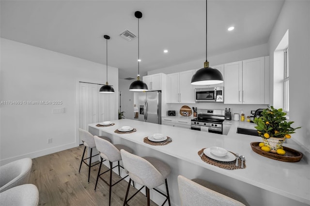kitchen featuring appliances with stainless steel finishes, light countertops, light wood-style flooring, a peninsula, and visible vents