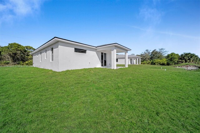 rear view of house featuring a lawn and stucco siding