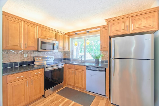 kitchen featuring light wood-style floors, a textured ceiling, tasteful backsplash, a sink, and stainless steel appliances