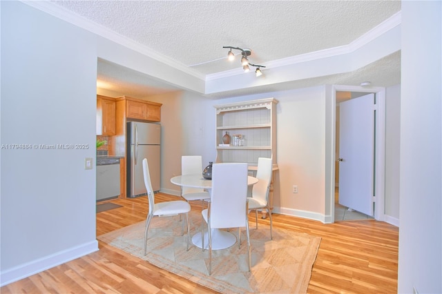 dining room featuring light wood-style floors, baseboards, ornamental molding, and a textured ceiling