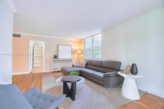 living area with a textured ceiling, light wood-style flooring, baseboards, visible vents, and ornamental molding