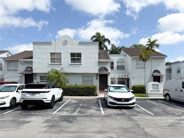 exterior space with a tiled roof, uncovered parking, and stucco siding