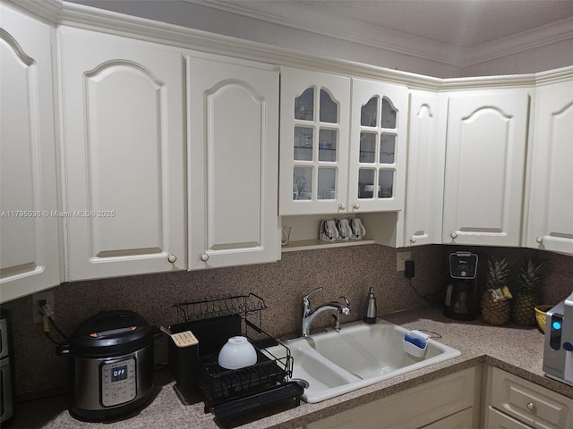 kitchen with decorative backsplash, crown molding, a sink, white cabinets, and glass insert cabinets