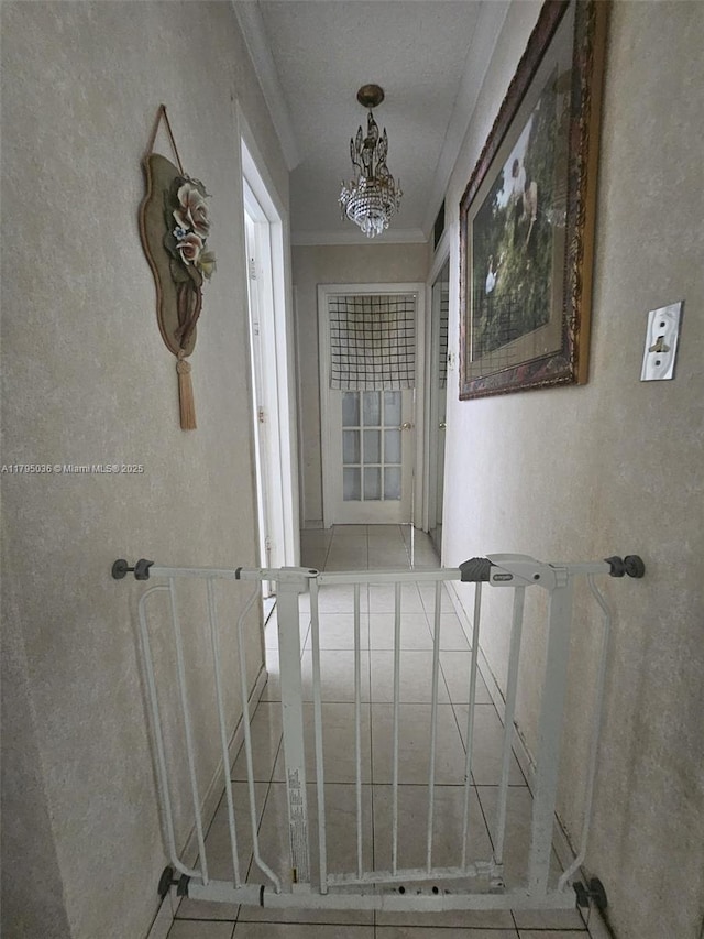corridor with ornamental molding, a textured wall, tile patterned floors, and a chandelier