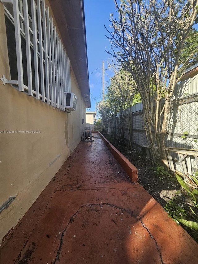 view of side of home featuring a wall mounted AC, fence, and stucco siding