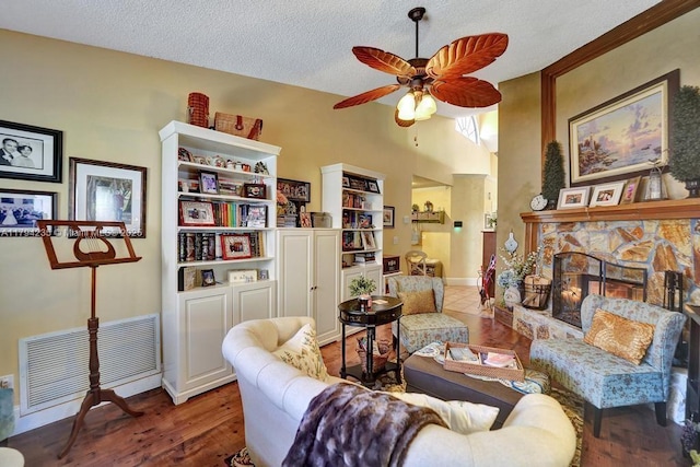 living room featuring a ceiling fan, a stone fireplace, a textured ceiling, visible vents, and wood finished floors