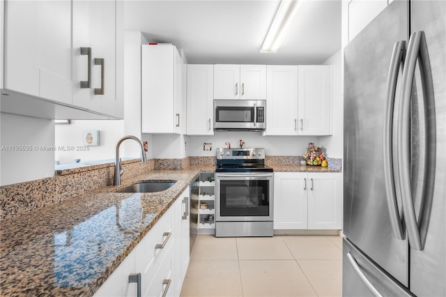 kitchen with a sink, white cabinets, light tile patterned floors, stone counters, and appliances with stainless steel finishes