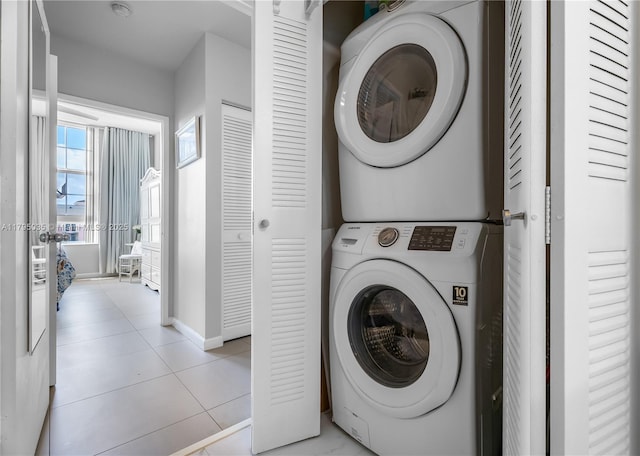 laundry area with laundry area, light tile patterned floors, baseboards, and stacked washer and dryer