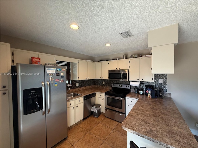 kitchen featuring stainless steel appliances, a sink, a textured ceiling, backsplash, and dark countertops