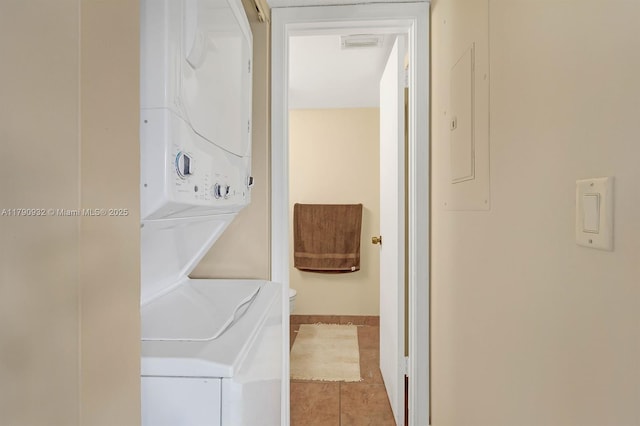laundry area featuring stacked washing machine and dryer, tile patterned floors, and baseboards