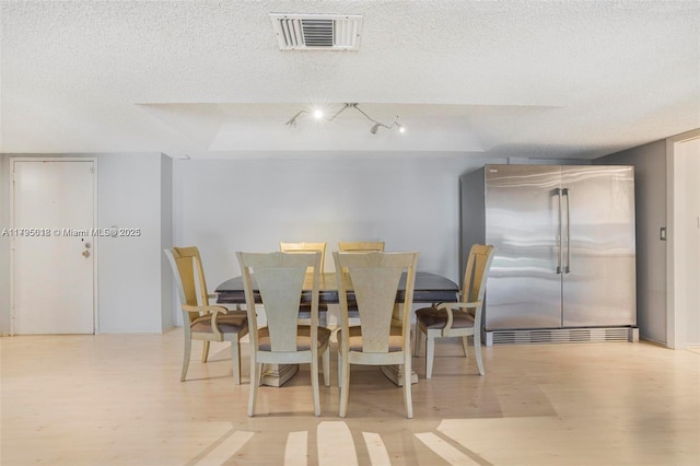 dining space featuring a textured ceiling, light wood-style flooring, and visible vents