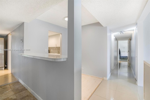 hall with baseboards, a textured ceiling, and light tile patterned floors