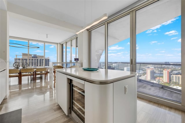 kitchen with wine cooler, a kitchen island, light countertops, floor to ceiling windows, and white cabinetry