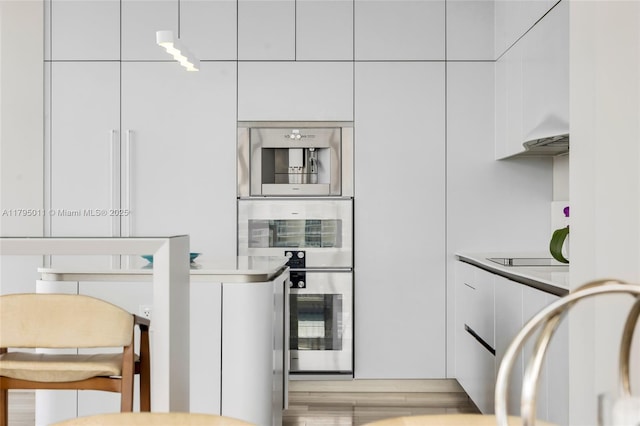 kitchen with double oven, modern cabinets, light countertops, black electric cooktop, and white cabinets
