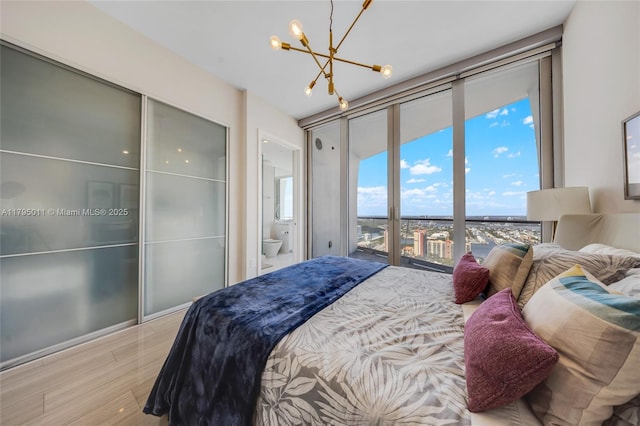 bedroom with ensuite bathroom, wood finished floors, and a notable chandelier