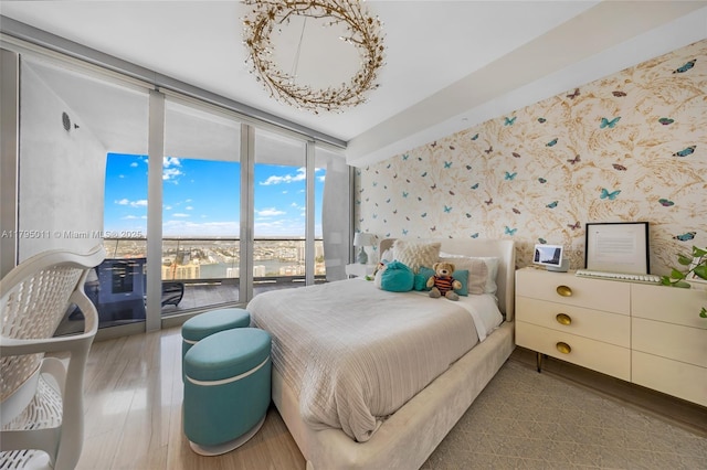 bedroom featuring floor to ceiling windows, wood finished floors, and wallpapered walls