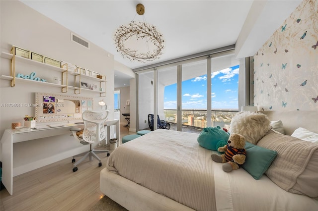 bedroom featuring a wall of windows, built in study area, baseboards, wood finished floors, and visible vents
