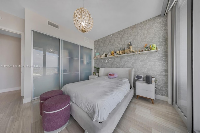 bedroom with a chandelier, an accent wall, baseboards, wallpapered walls, and visible vents