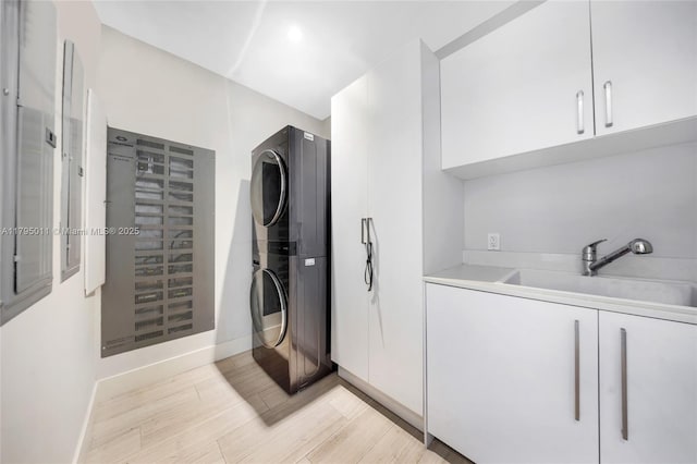 laundry area featuring cabinet space, a sink, baseboards, light wood finished floors, and stacked washer and clothes dryer
