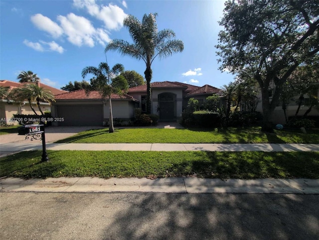mediterranean / spanish-style home with a garage, stucco siding, a front yard, a tiled roof, and driveway