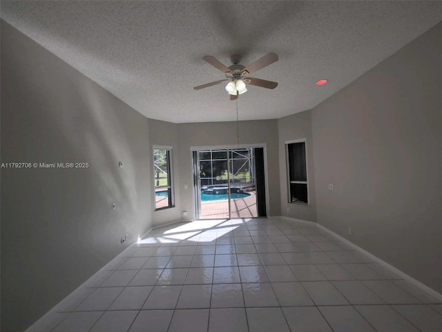 empty room featuring baseboards, light tile patterned floors, a textured ceiling, and ceiling fan