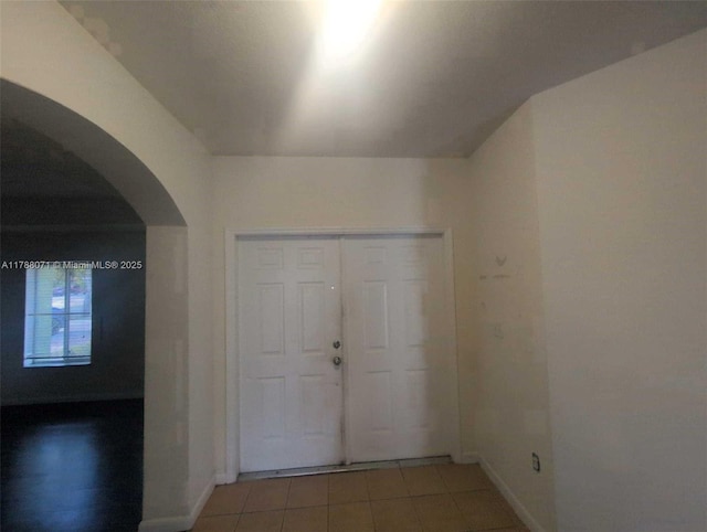 entryway featuring baseboards, arched walkways, and light tile patterned floors