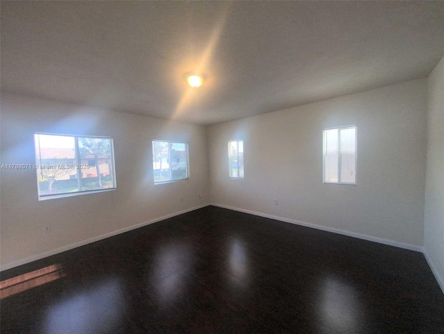 unfurnished room with baseboards, dark wood-style floors, and a wealth of natural light