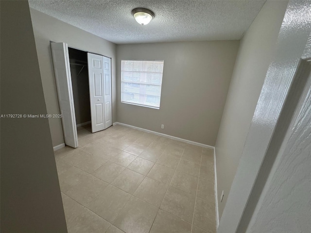 unfurnished bedroom with light tile patterned floors, baseboards, a closet, and a textured ceiling