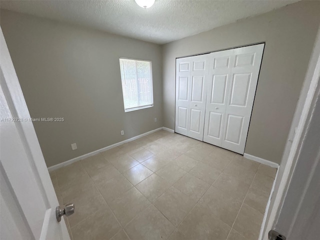 unfurnished bedroom with baseboards, a closet, a textured ceiling, and light tile patterned flooring