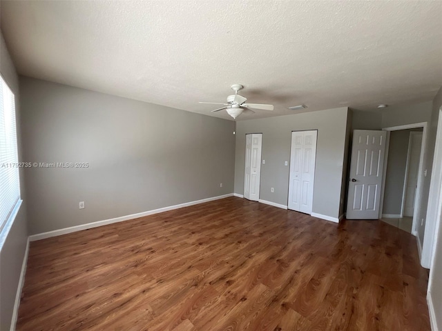 unfurnished bedroom featuring baseboards, ceiling fan, two closets, and wood finished floors