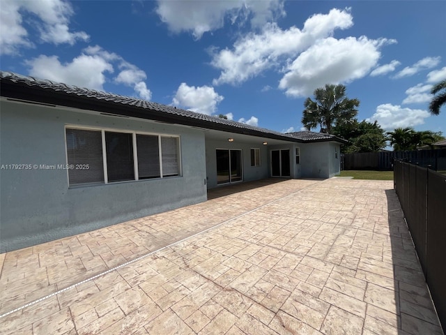 back of property with stucco siding, a patio area, fence, and a tile roof