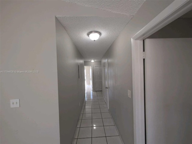 corridor featuring light tile patterned flooring, a textured ceiling, and baseboards