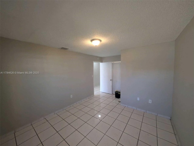 unfurnished room featuring visible vents, a textured ceiling, light tile patterned floors, and baseboards