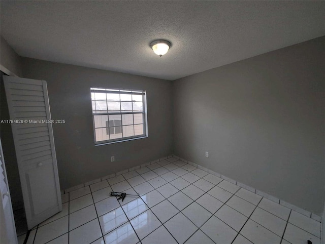 empty room with a textured ceiling and light tile patterned floors