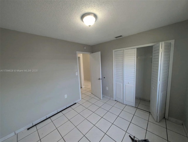unfurnished bedroom with a textured ceiling, baseboards, light tile patterned floors, visible vents, and a closet