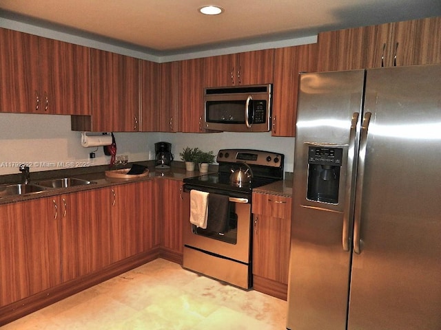 kitchen featuring brown cabinetry, a sink, appliances with stainless steel finishes, and dark countertops
