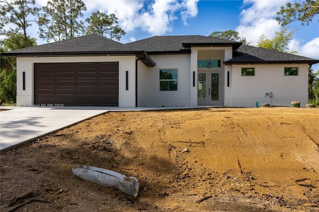 prairie-style house featuring french doors, roof with shingles, a garage, concrete driveway, and stucco siding