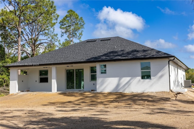 rear view of property featuring central AC unit, roof with shingles, and stucco siding