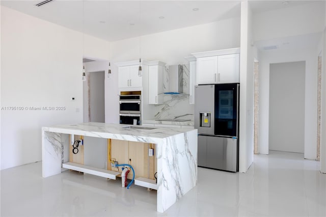 kitchen with light stone countertops, a center island, wall chimney exhaust hood, white cabinets, and appliances with stainless steel finishes